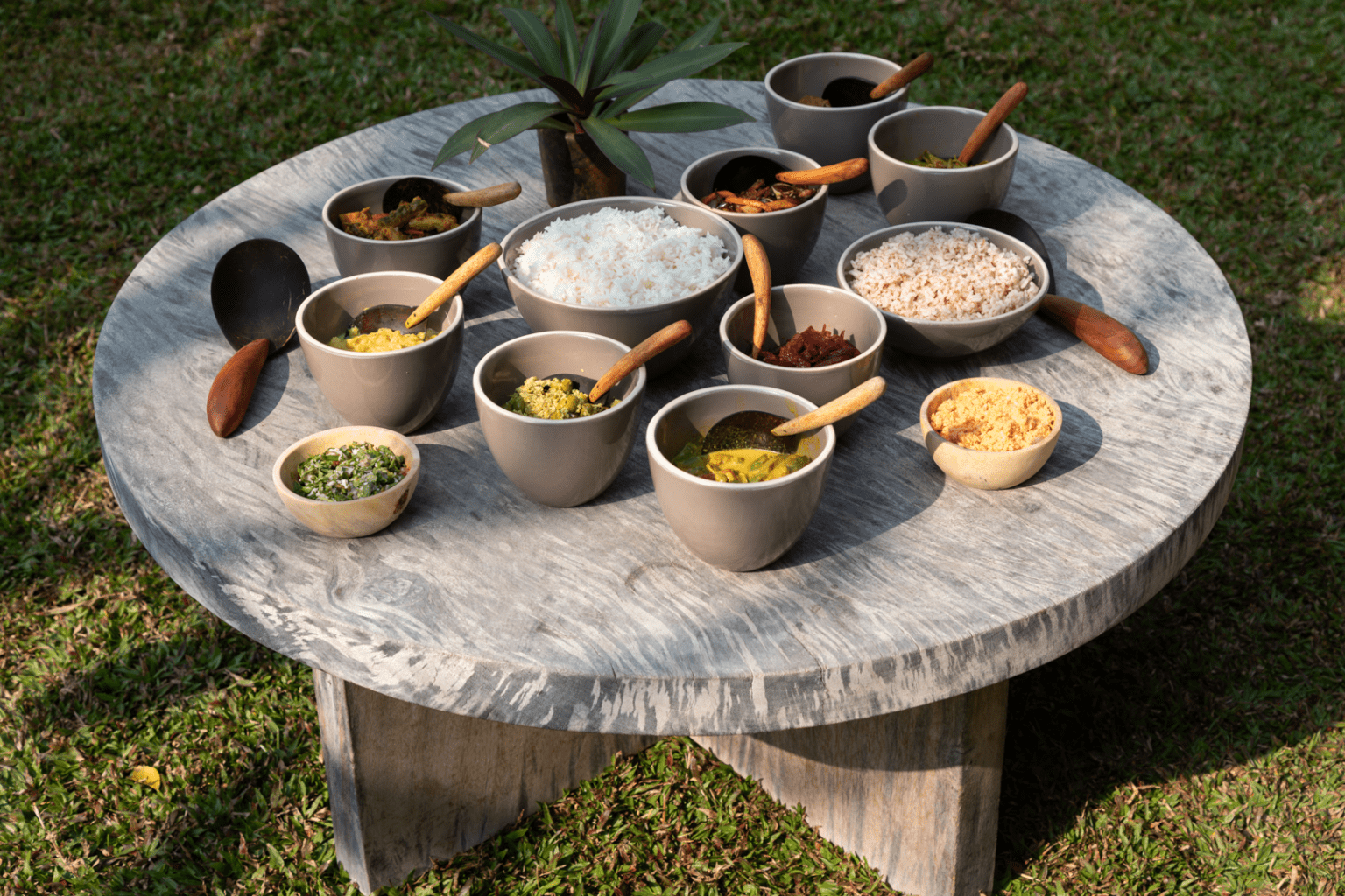 A round stone table on the lawn set with bowls of rice, grains and spices